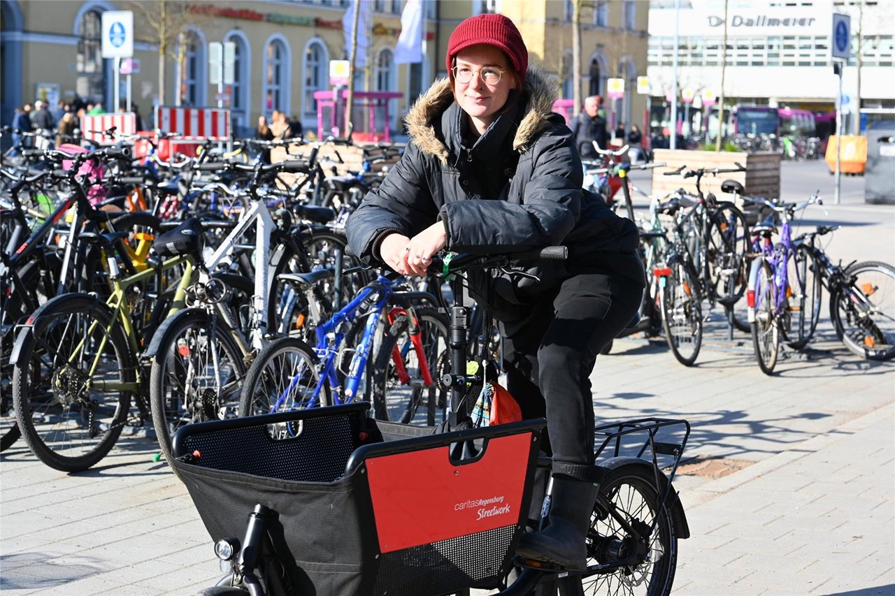 Olivia Mantwill sitzt auf einem Lastenfahrrad. im Hintergrund sieht man den Bahnhof und weitere Fahrräder.
