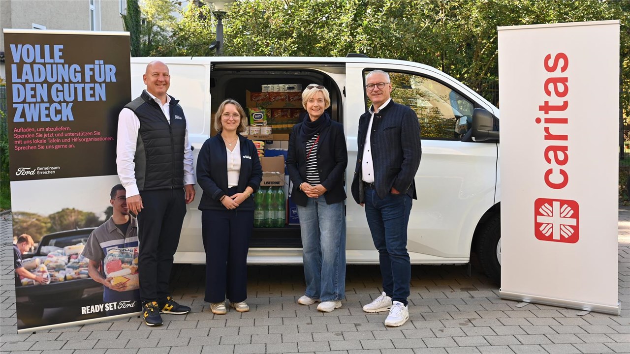 Vier Menschen stehen vor einem weißen Ford Transit. Rechts und links im Bild stehen zwei Roll-Ups